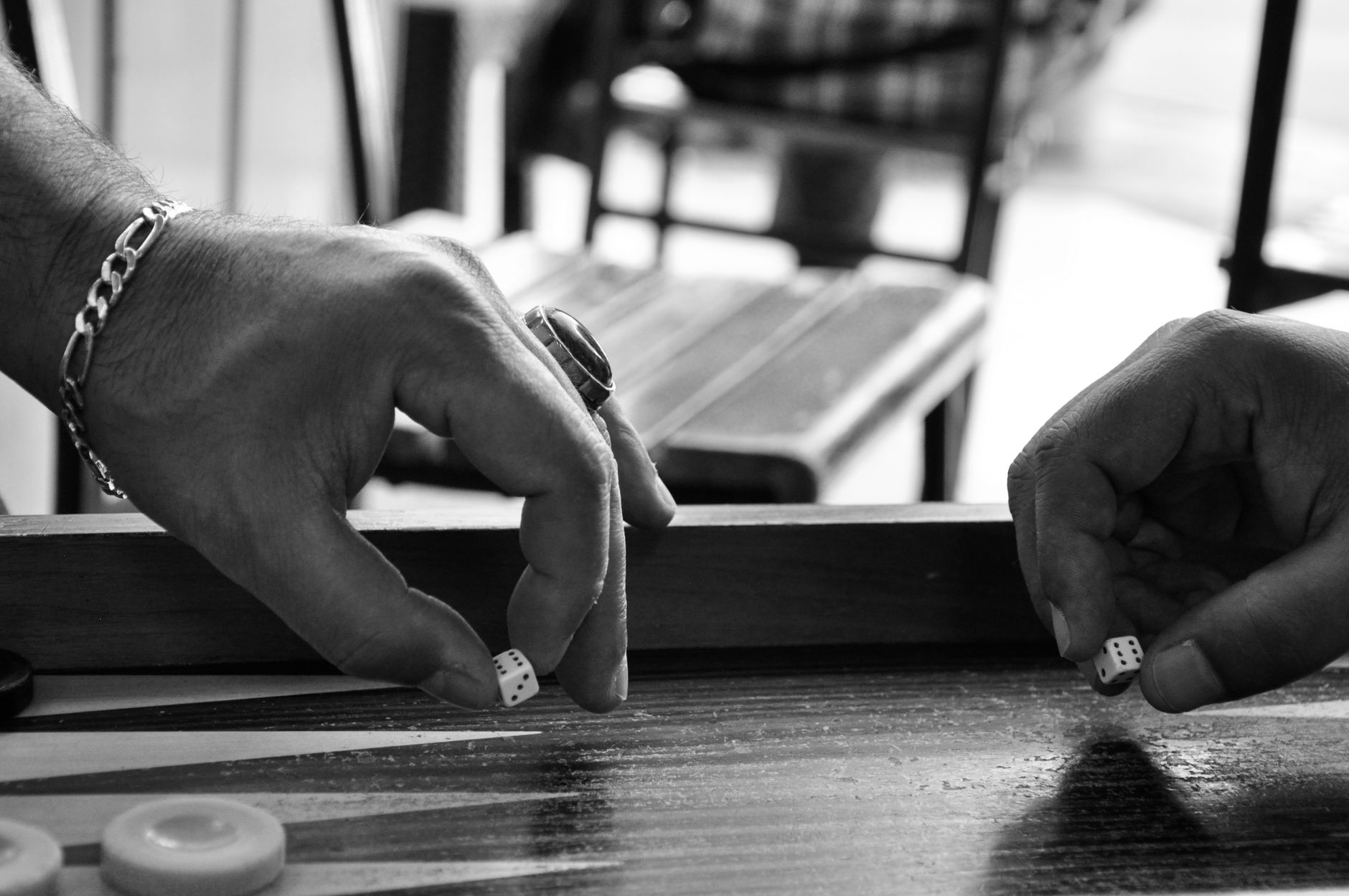 Black and white image of two people playing backgammon, focusing on hands and dice.