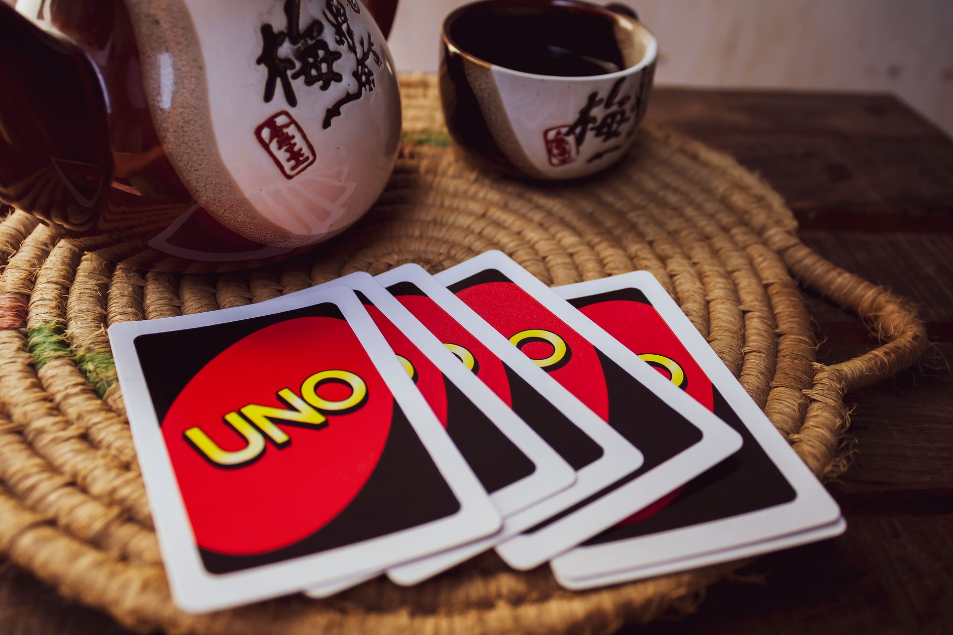 Close-up of UNO cards with a traditional teapot and cup on a woven mat. Warm and cozy indoor setting.