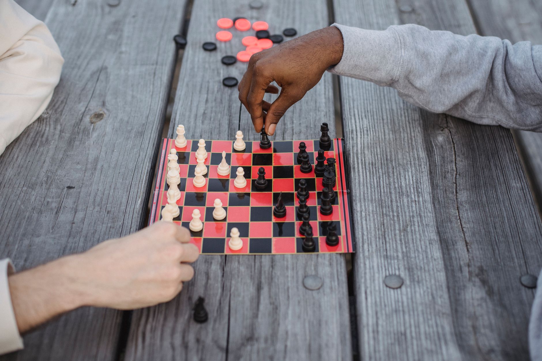 From above of crop anonymous multiethnic friends playing chess sitting at wooden table