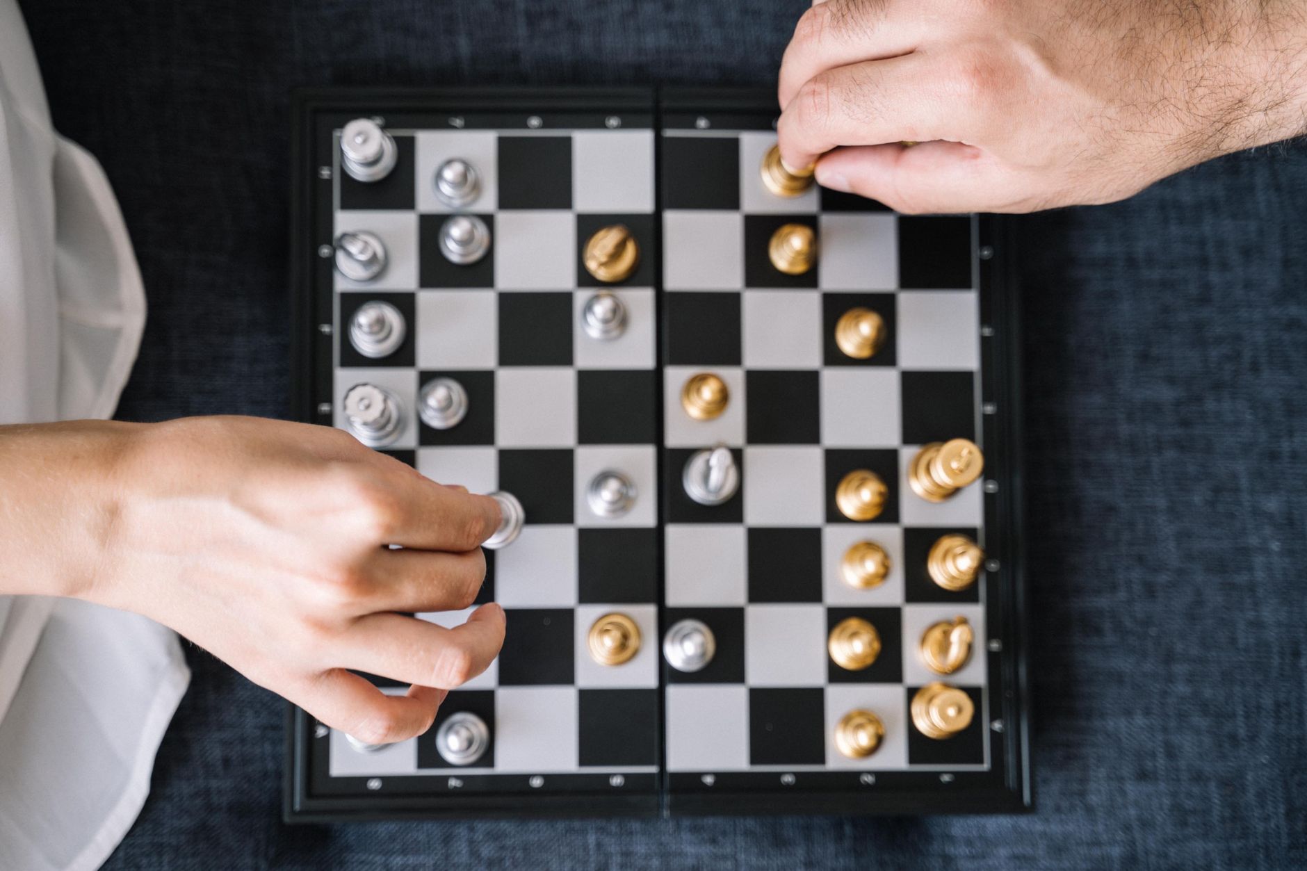 Close-up of a chess game in progress with hands moving pieces on the chessboard.