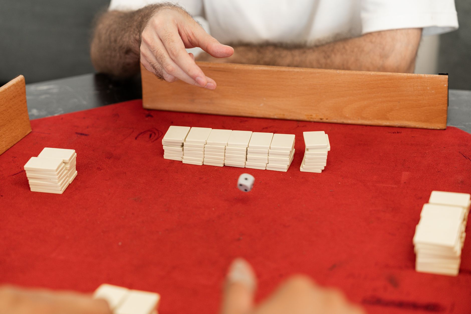 Two people enjoy a board game with dice and tiles on a red table indoors.