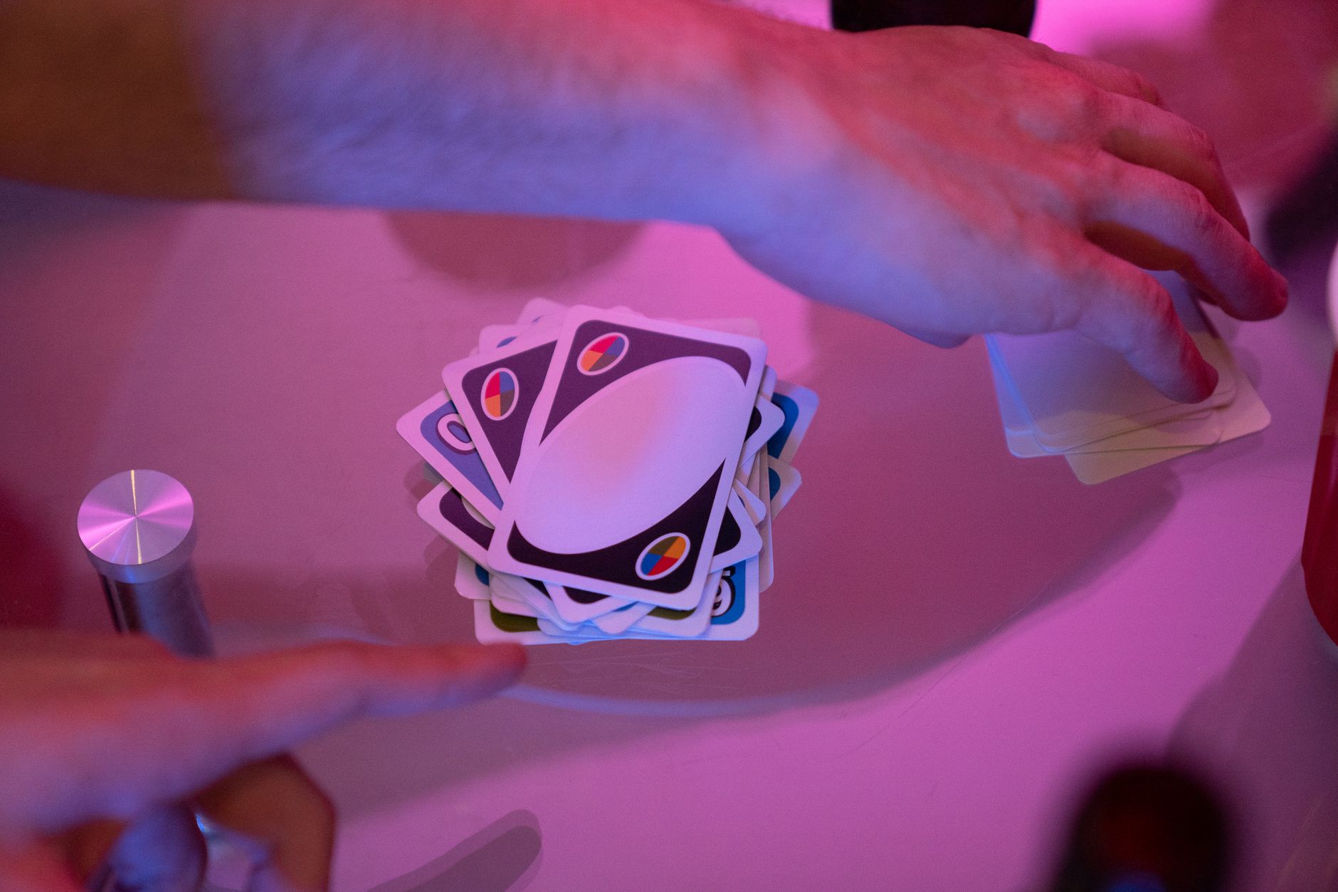 Close-up of hands engaged in a game of cards with vibrant lighting on a table.