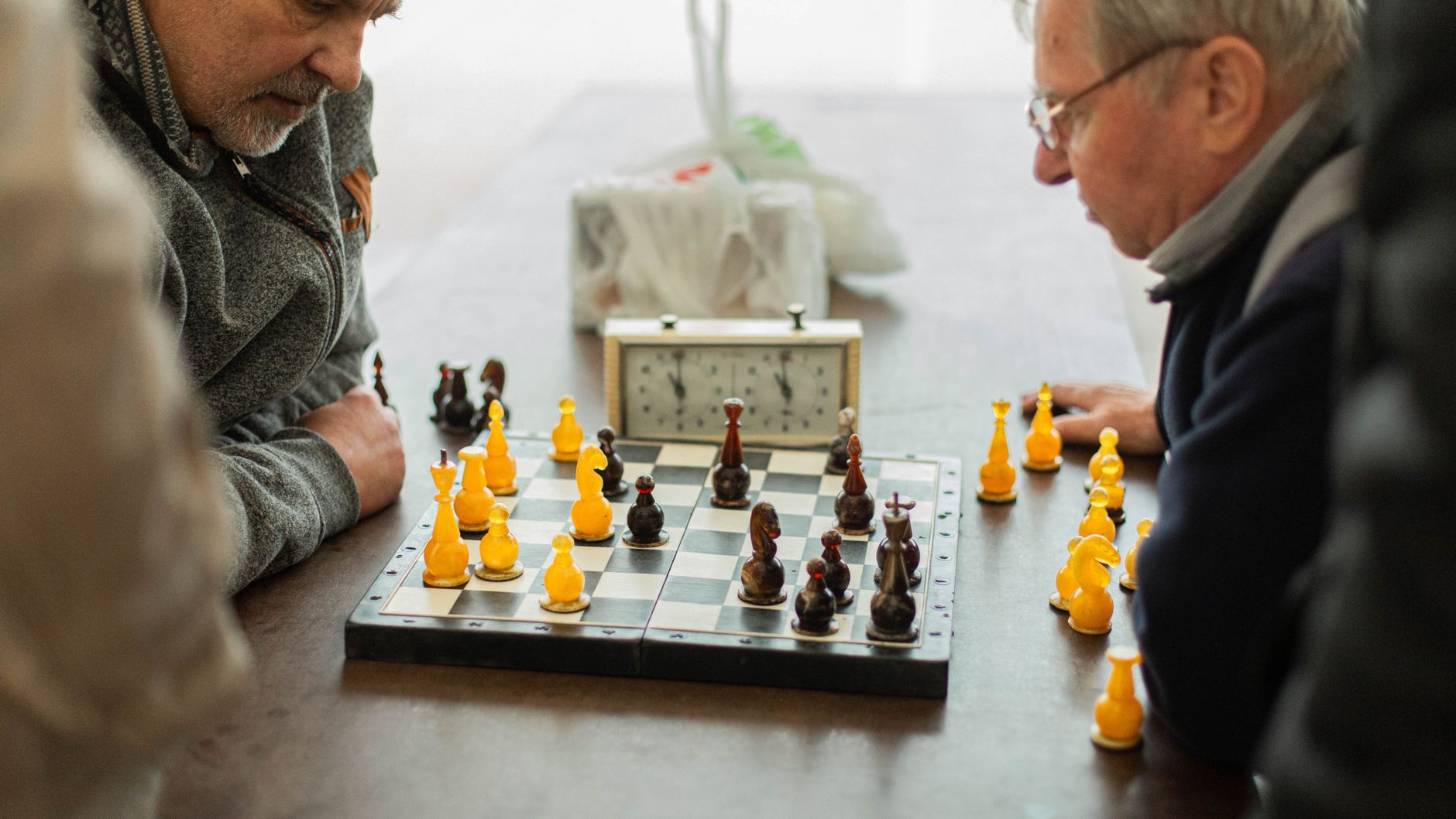Two elderly men engaged in a game of chess at a table indoors, focusing on strategy.