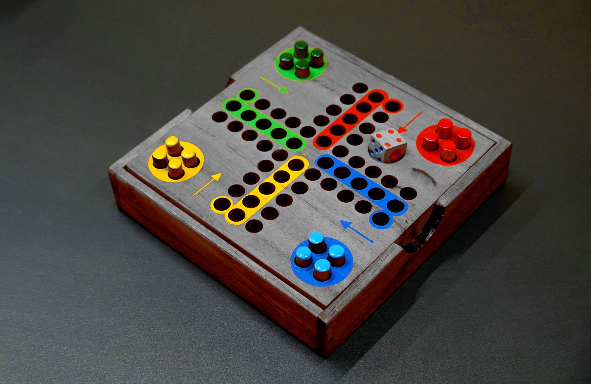 A vibrant wooden board game with colorful pieces and a die on a dark surface.