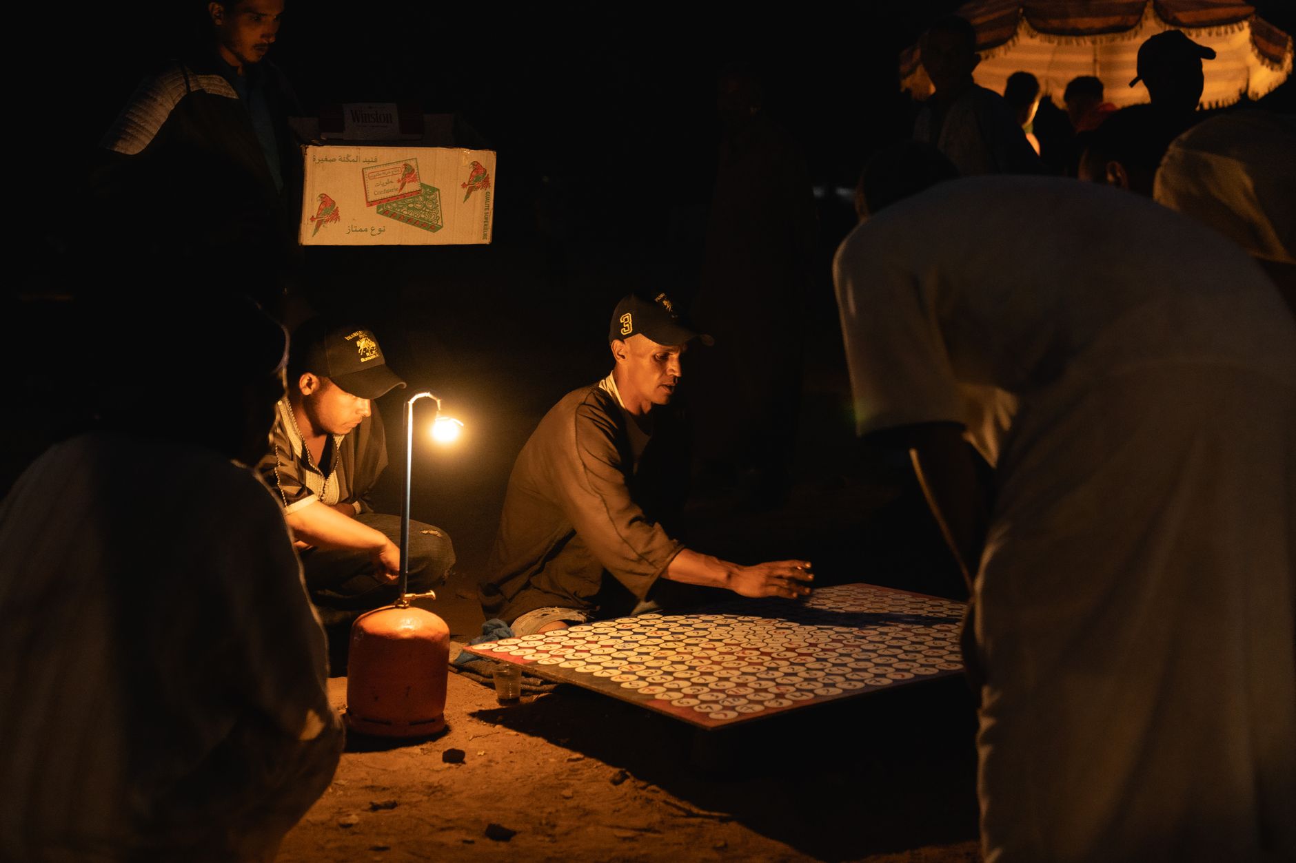 Men play a board game by lamplight in Tiznit, Morocco. Captivating nighttime scene.