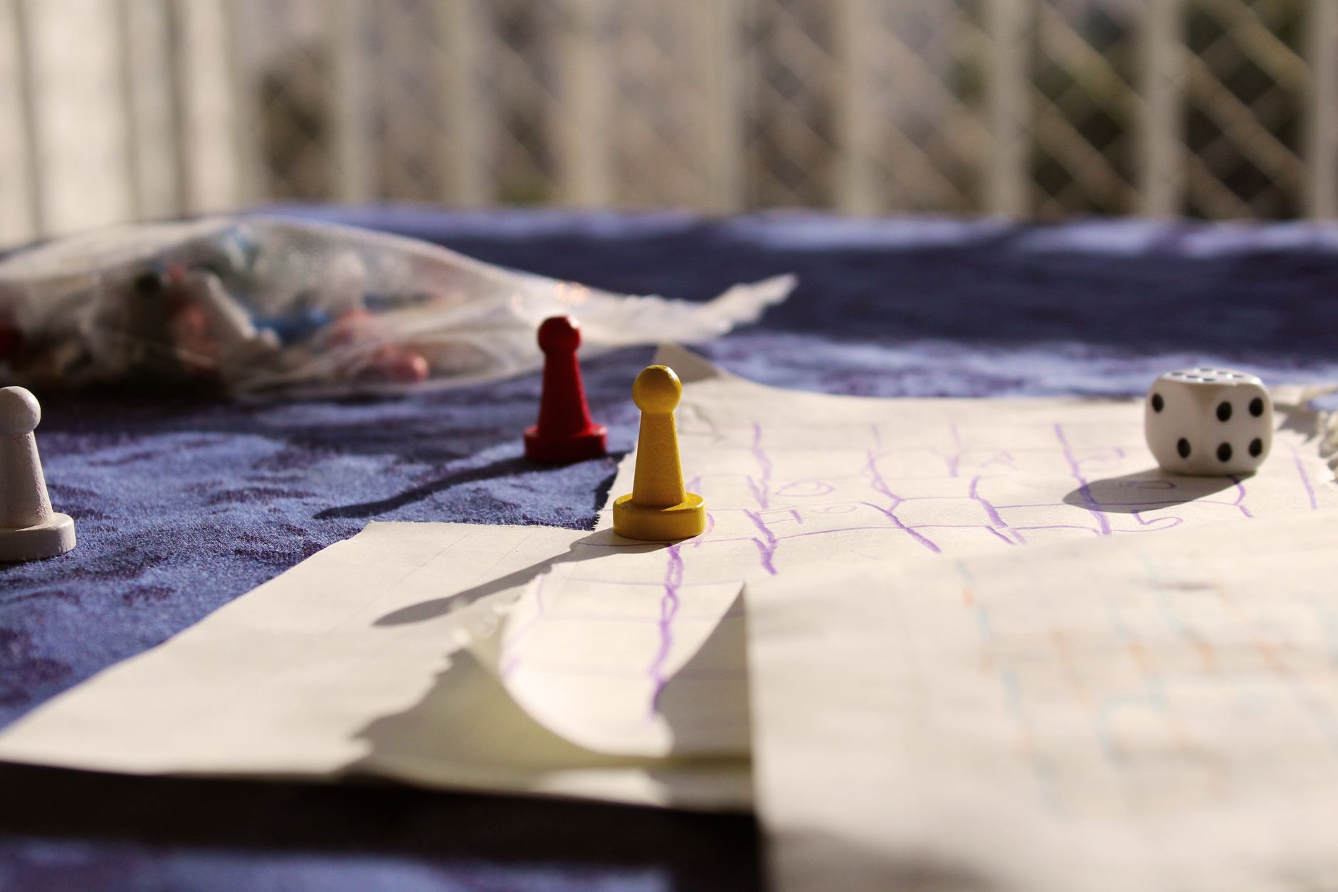 Close-up of colorful game pawns and a dice on a paper board under sunlight.