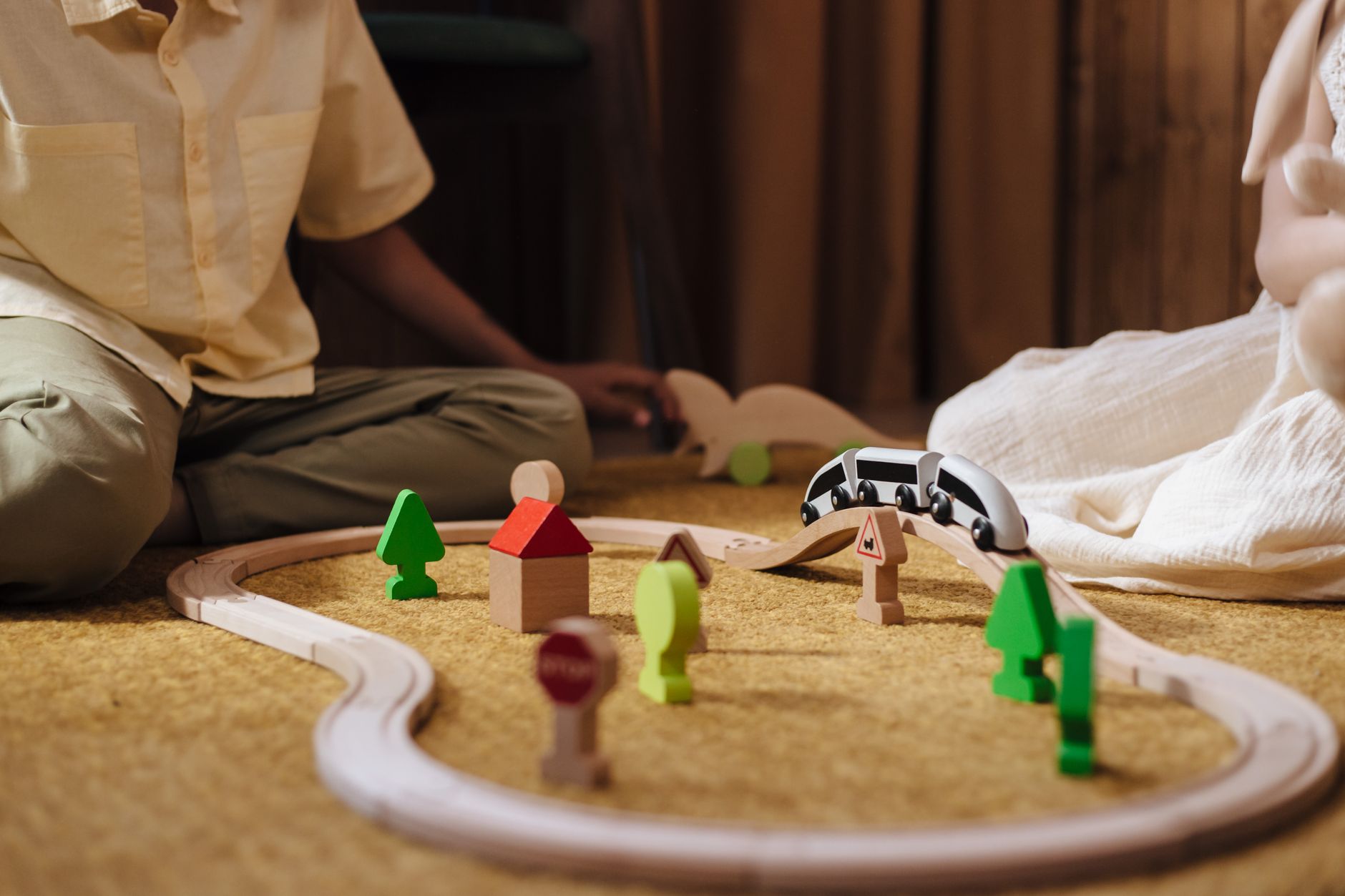 Two children playing with a colorful wooden train set on a carpet indoors, fostering creativity.