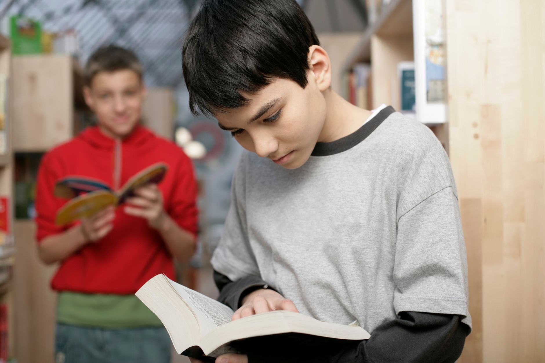 Two boys reading books in a library, enhancing their knowledge and learning experience.