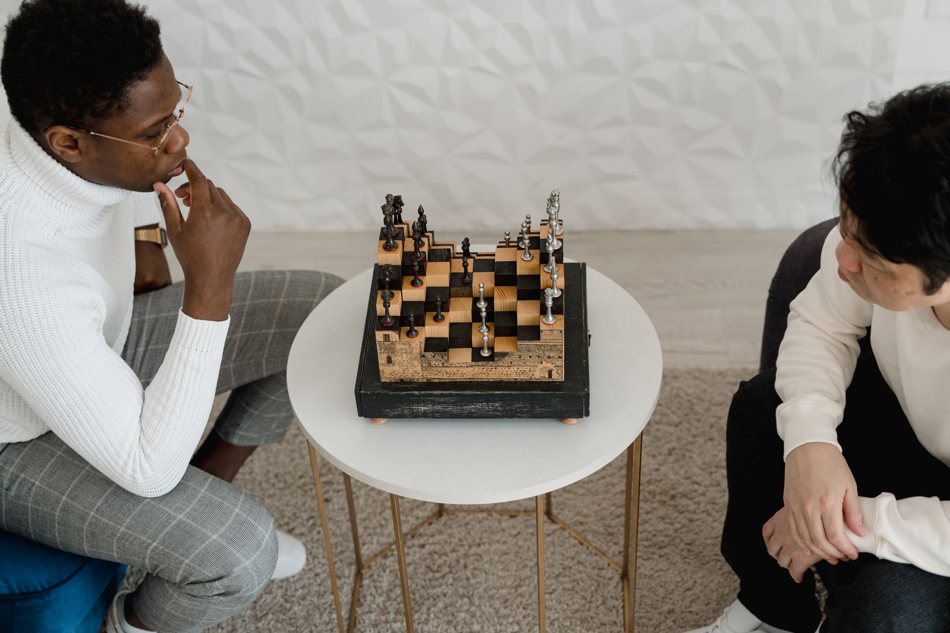 Two adults thoughtfully play a chess game indoors, focusing on their next strategic move.