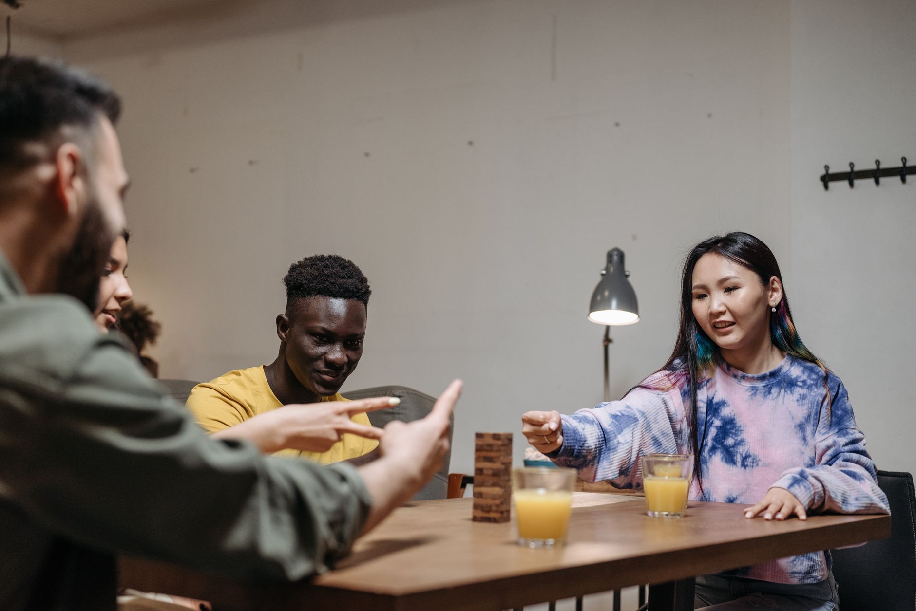 Diverse group of friends playing a game indoors with drinks, creating a lively atmosphere.