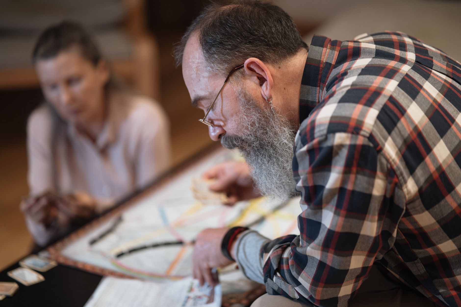 A bearded man and a woman engaging in an intense board game at home. Captured indoors.