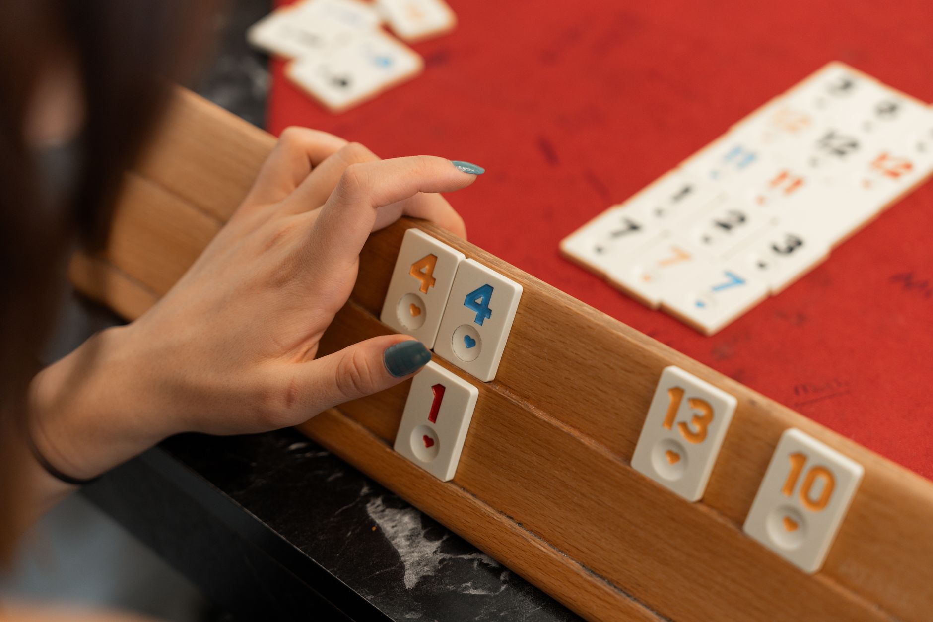 A person playing Rummikub indoors in Yalova, Türkiye. A close-up shot of a hand arranging tiles on a game rack.