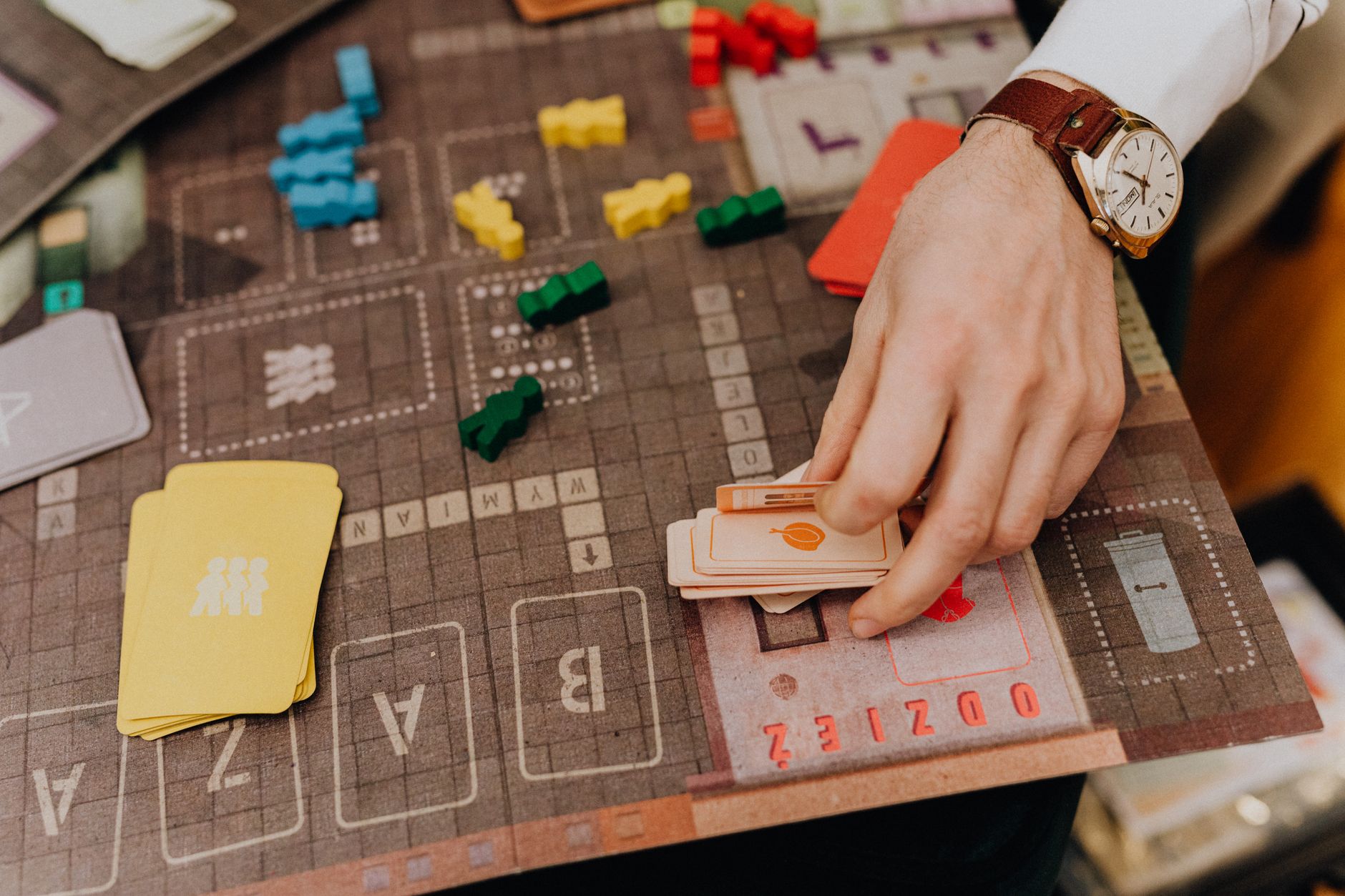 Close-up of a hand playing a board game with cards and colorful pawns.