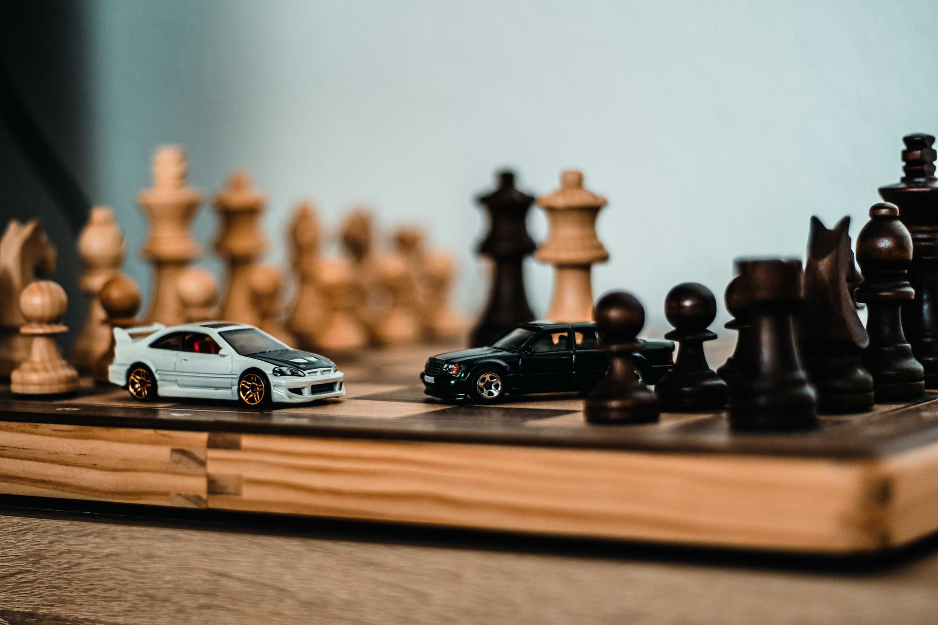 Model cars placed on a wooden chessboard, merging hobbies of model collecting and chess.