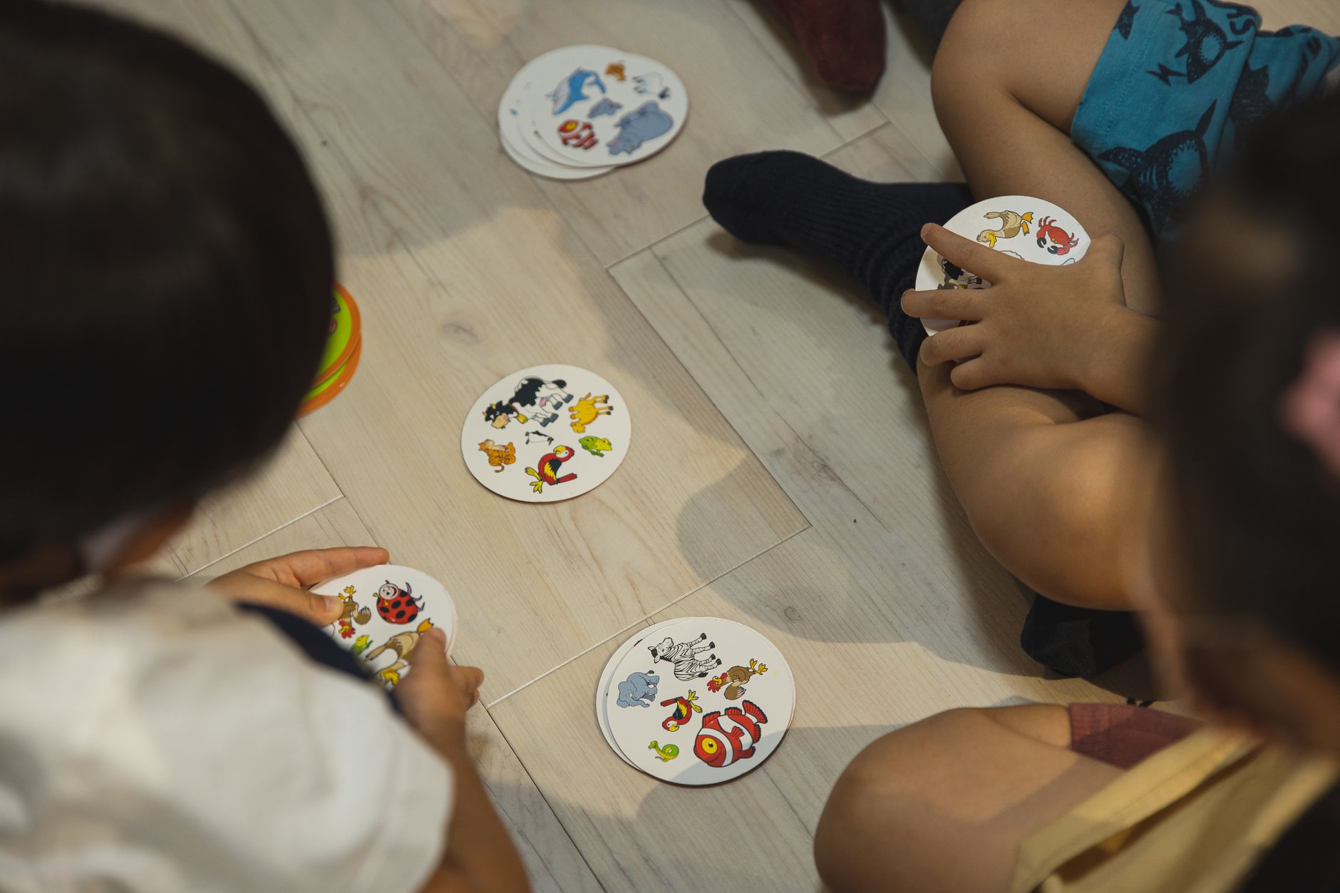From above of crop anonymous preschool ethnic kids sitting with crossed legs with round shape cards while playing on floor