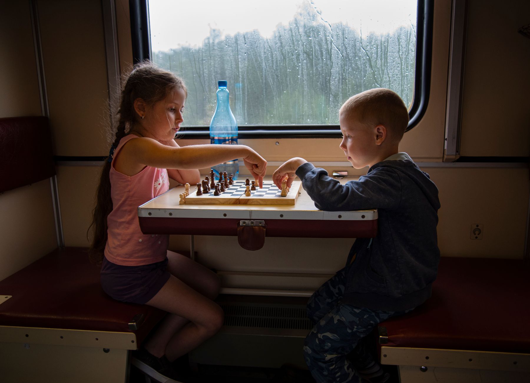 Two children play chess in a cozy train compartment in Russia during daytime.