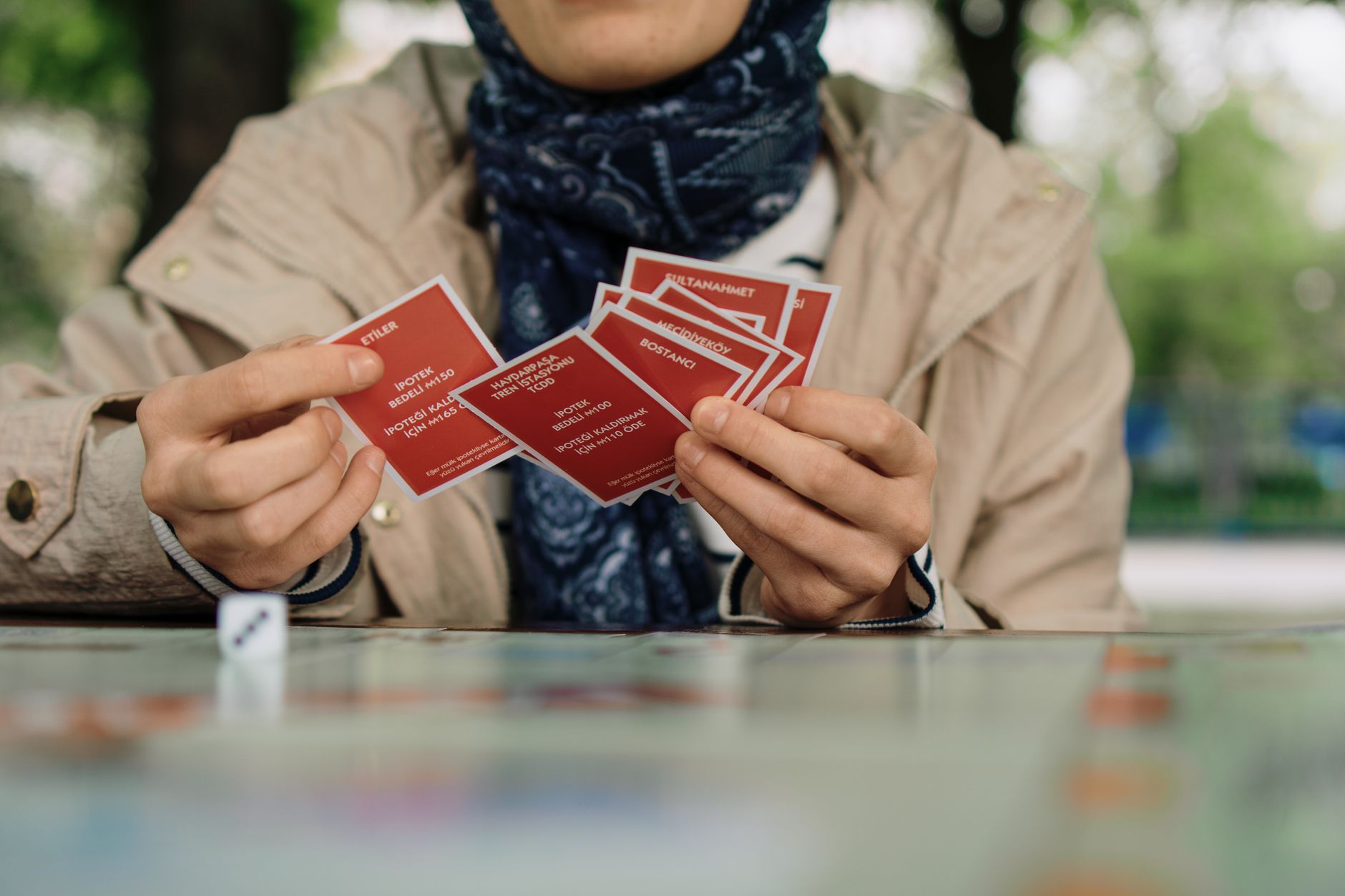 Close-up of a woman holding cards while playing a board game outdoors in a park.
