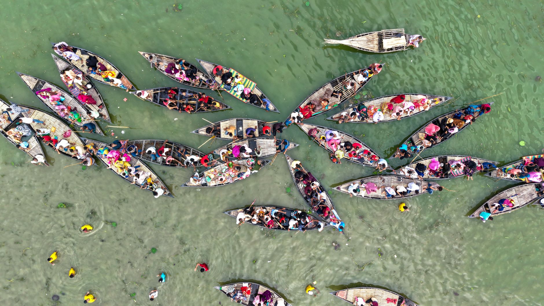 Aerial shot capturing vibrant wooden boats on a river, filled with people and activities.