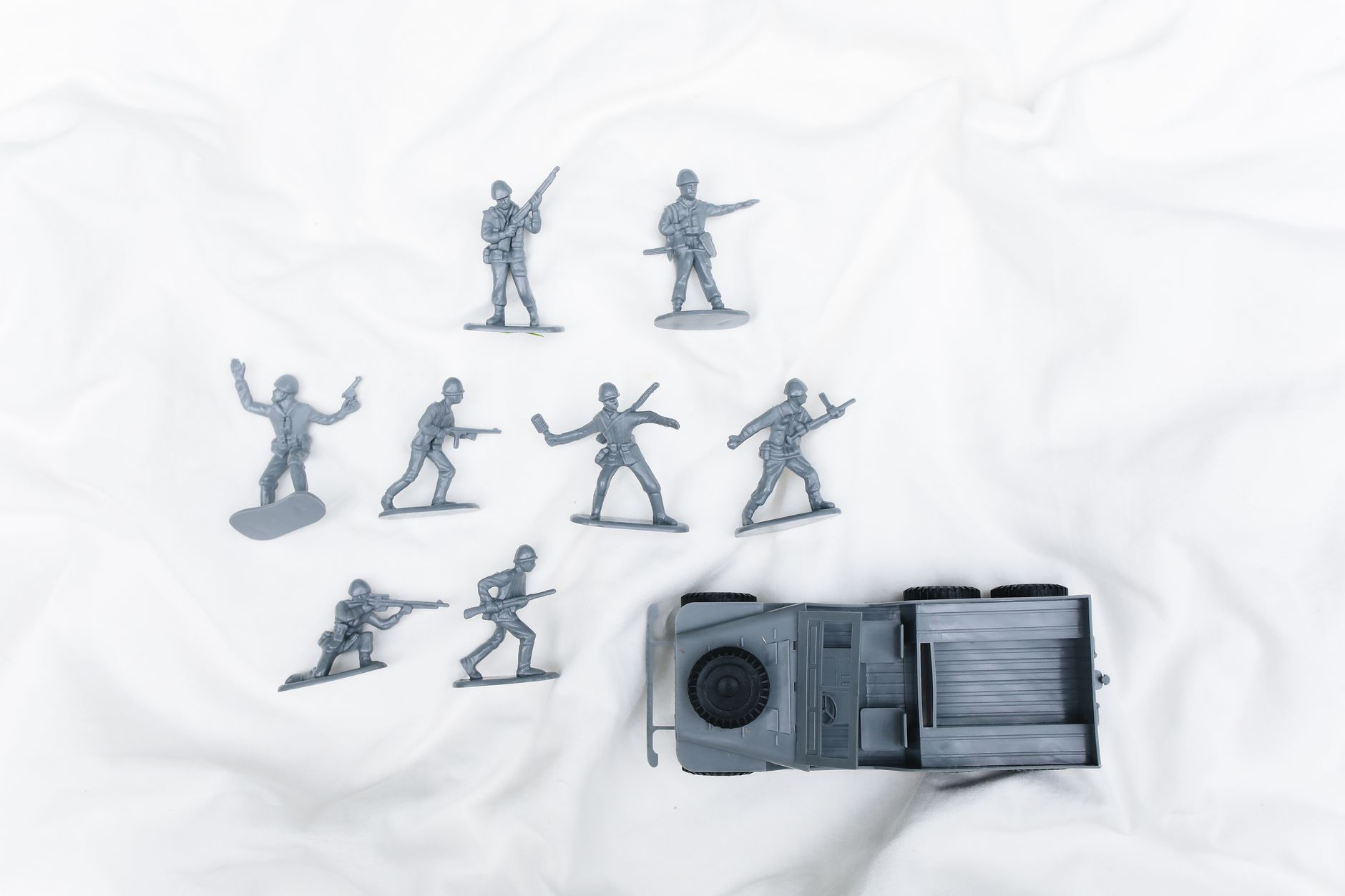 Army toy soldiers in action poses with a jeep on a plain white surface, perfect for military-themed projects.