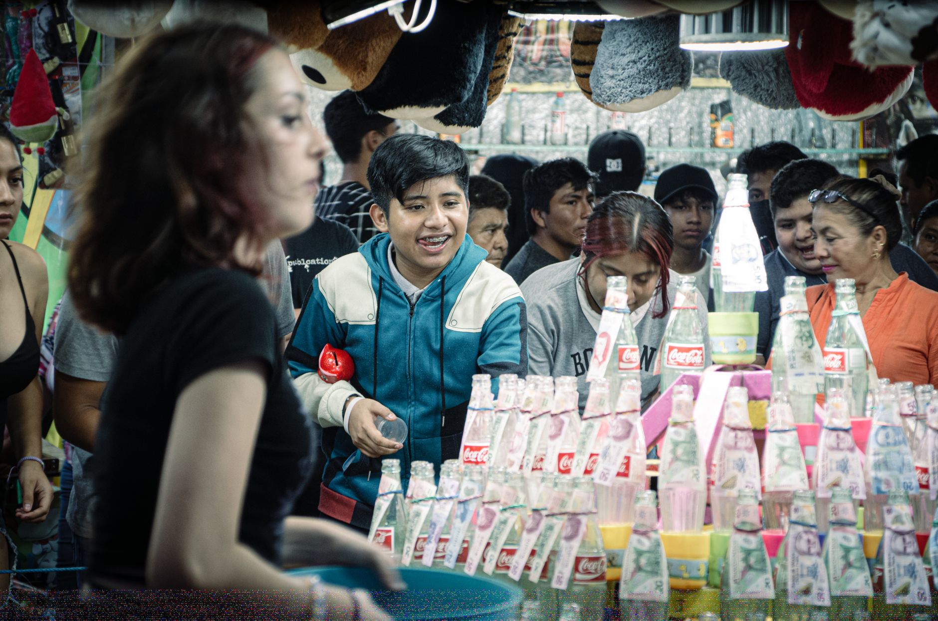 A dynamic fairground scene showing a variety of people playing games amidst bottles and prizes.