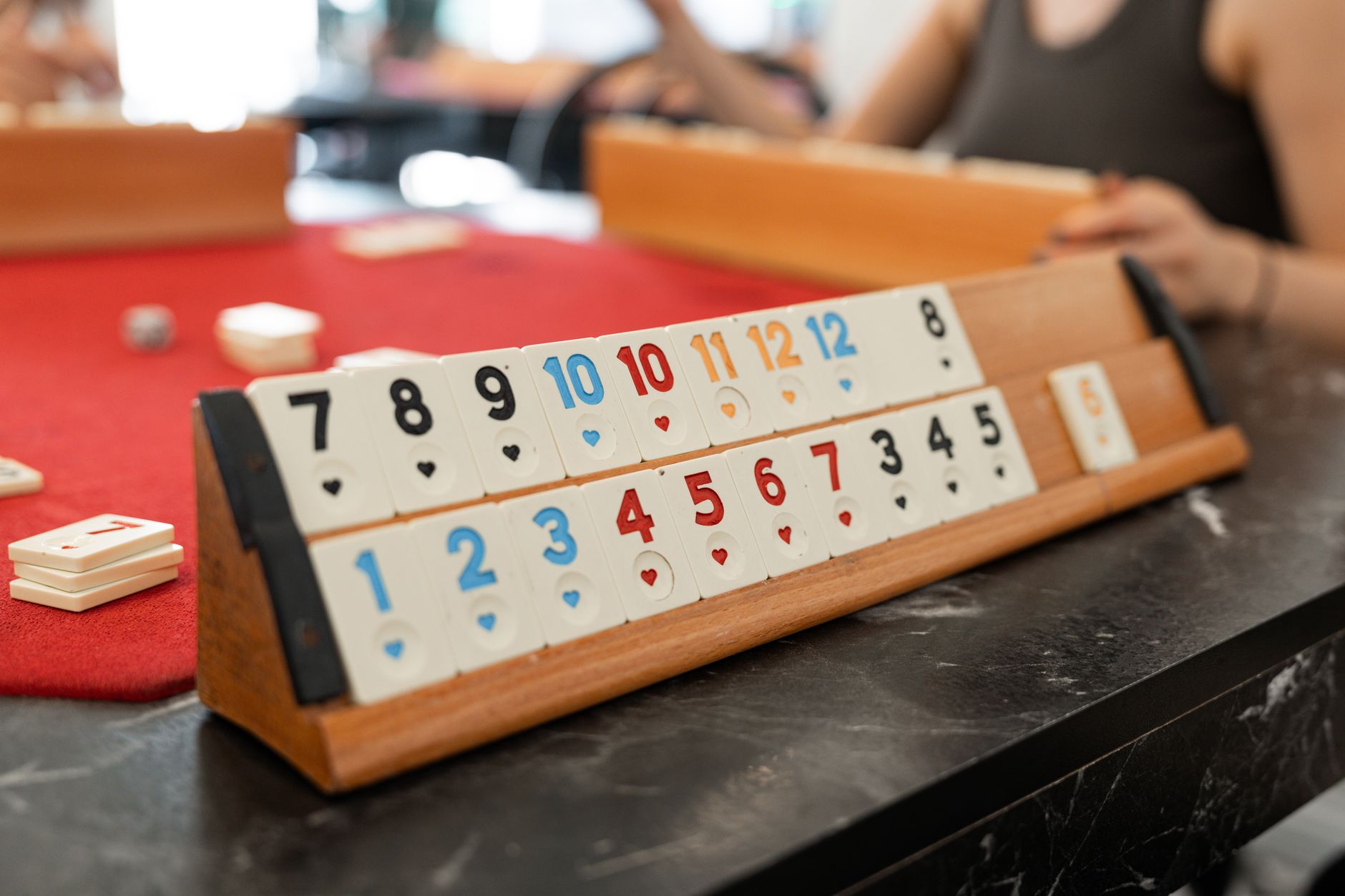 Colorful Rummikub tiles arranged on a wooden rack during an indoor game session.