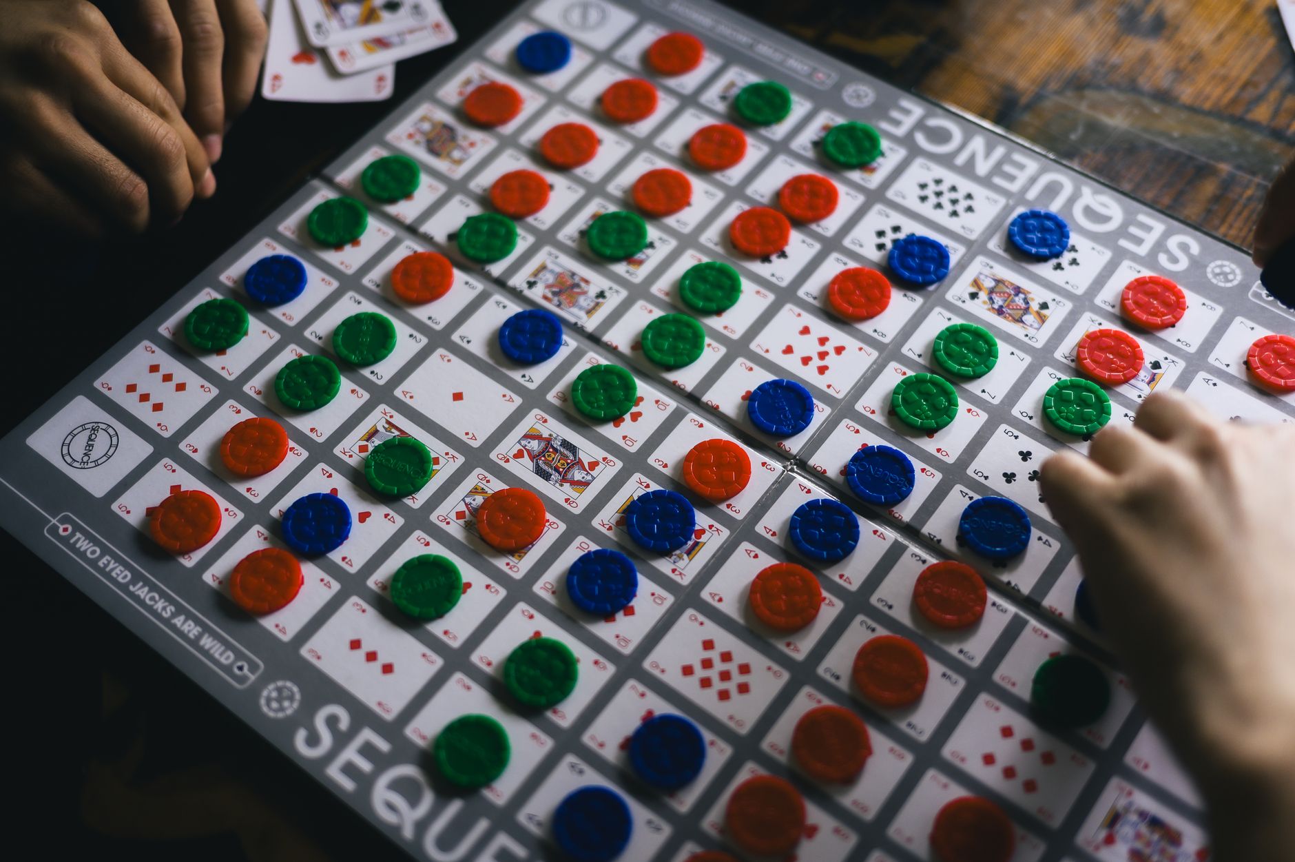 Players engaged in a game of Sequence, strategizing with colorful chips.