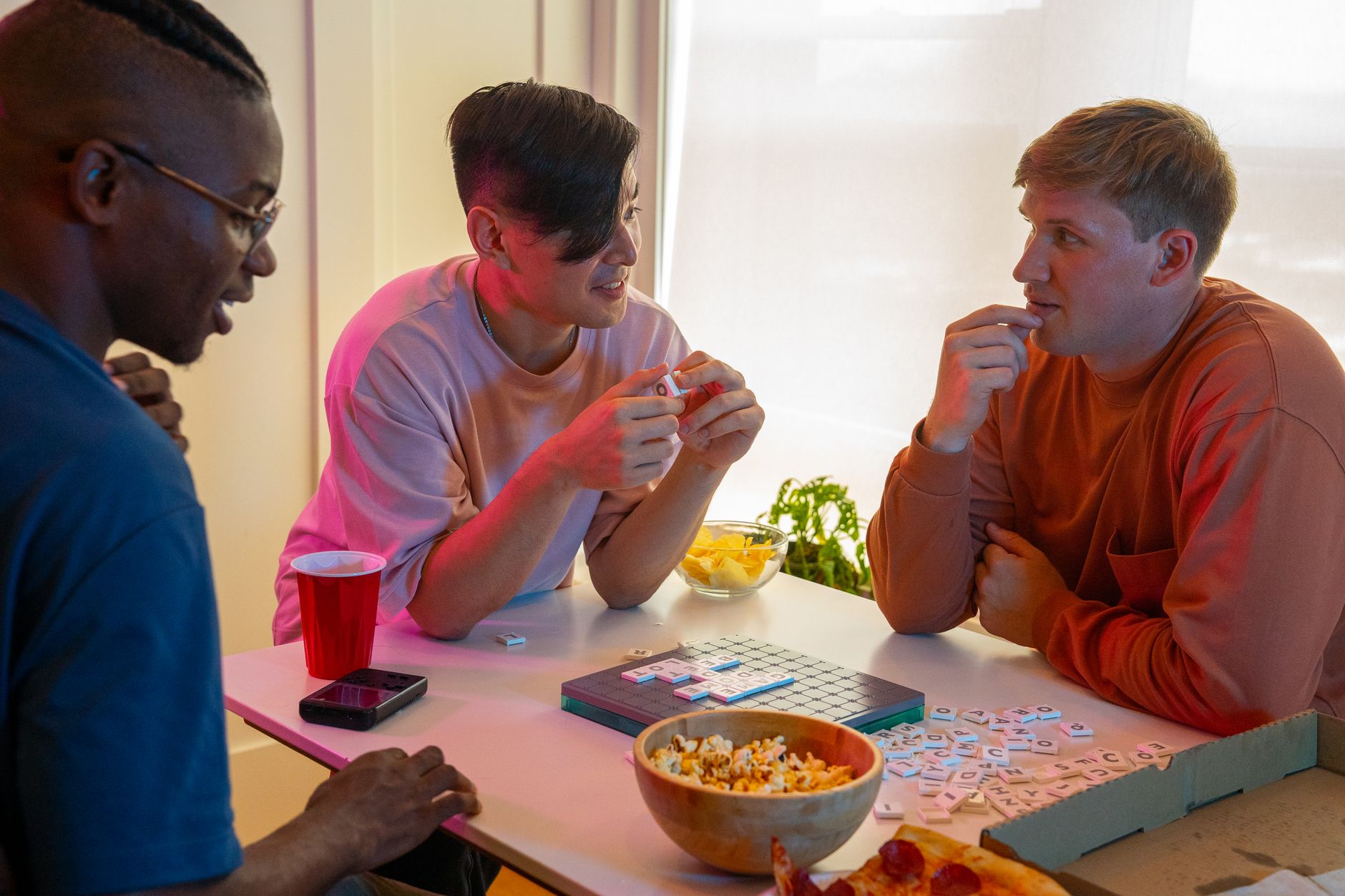 Three friends engaged in a board game, enjoying snacks and a cozy atmosphere at home.
