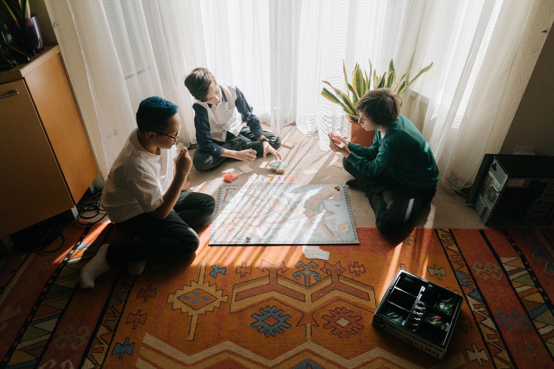 Three kids enjoy a board game afternoon in a cozy, sunlit room, fostering strategic play.