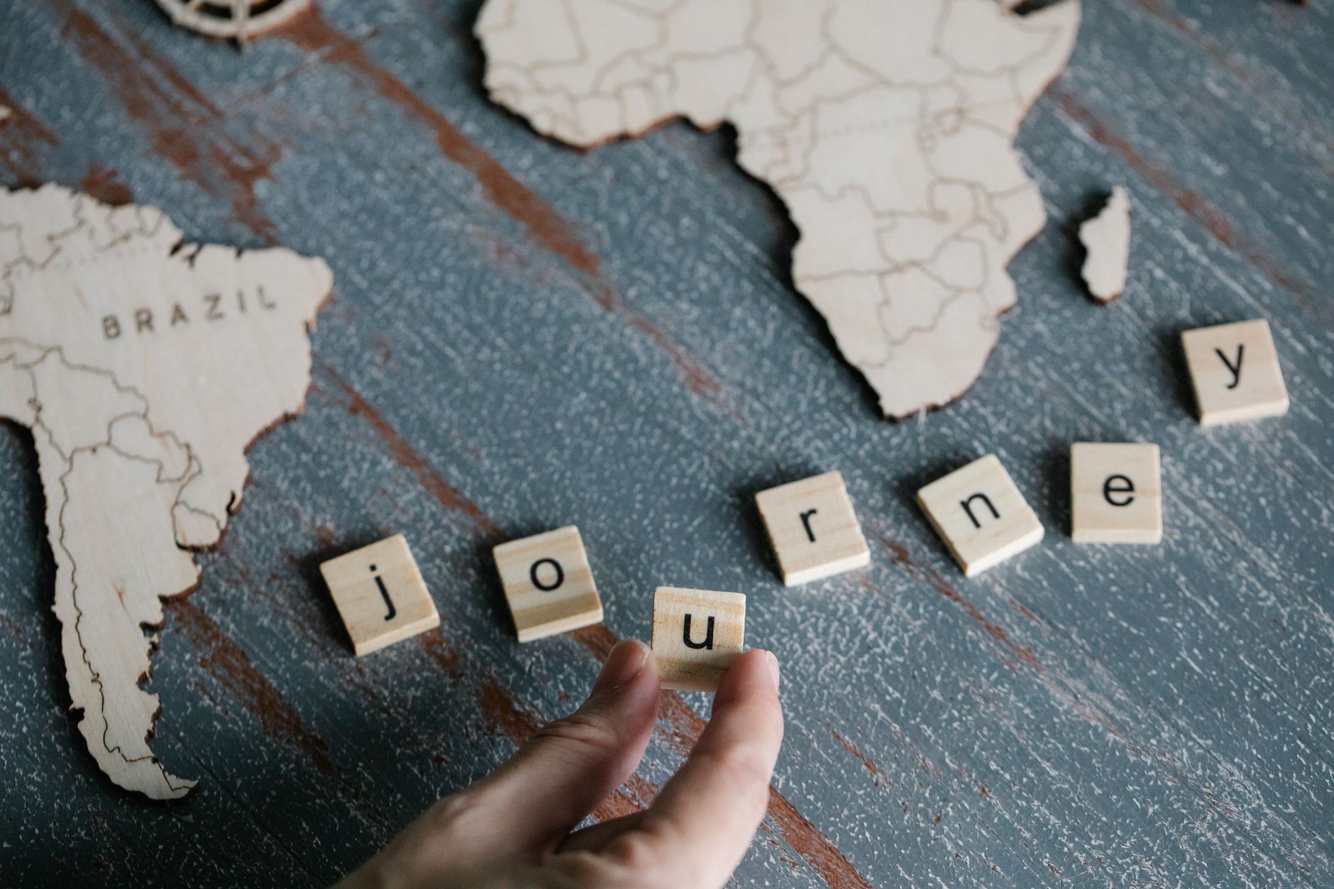 Wooden blocks spelling 'journey' with map cutouts of Brazil and Africa on a table.