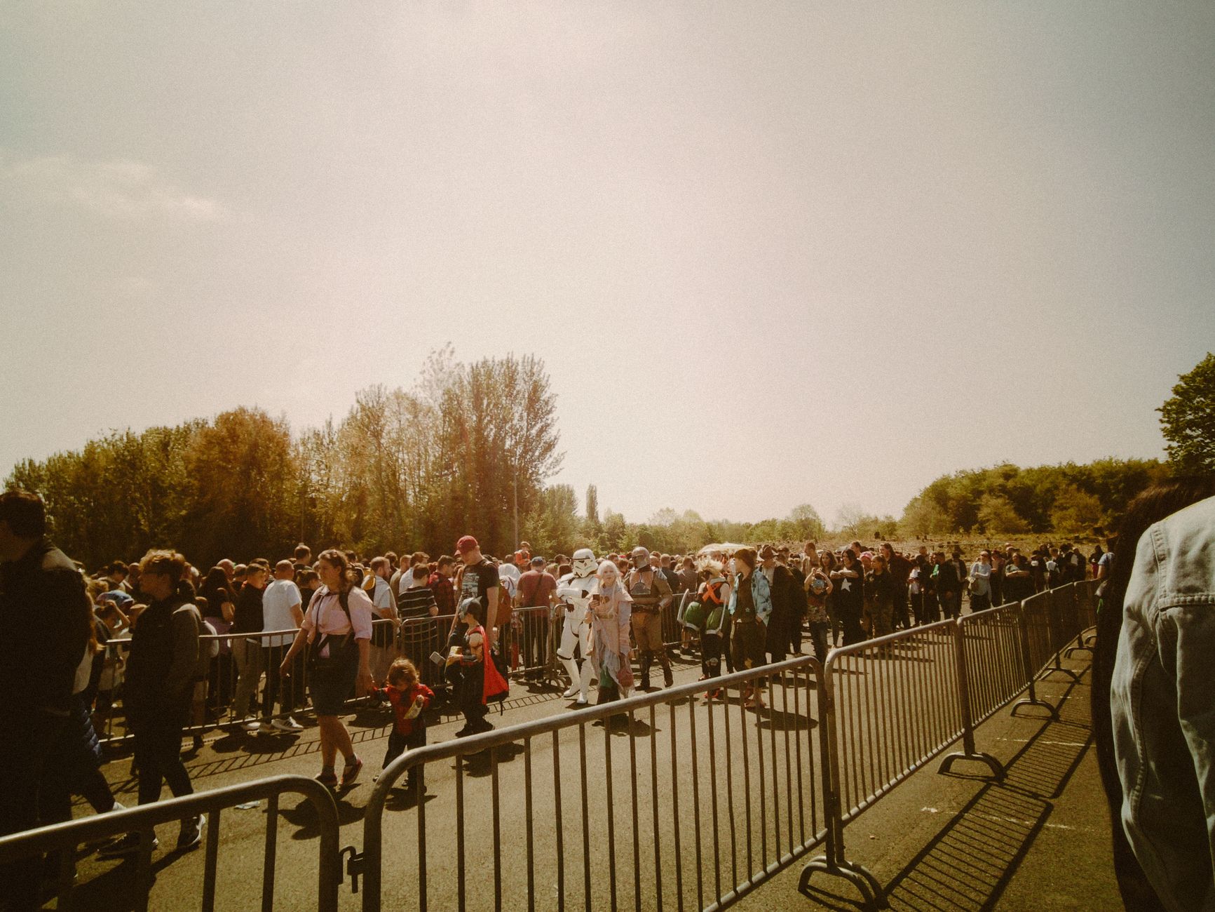 A large crowd in costumes waits in line at an outdoor festival on a sunny day.