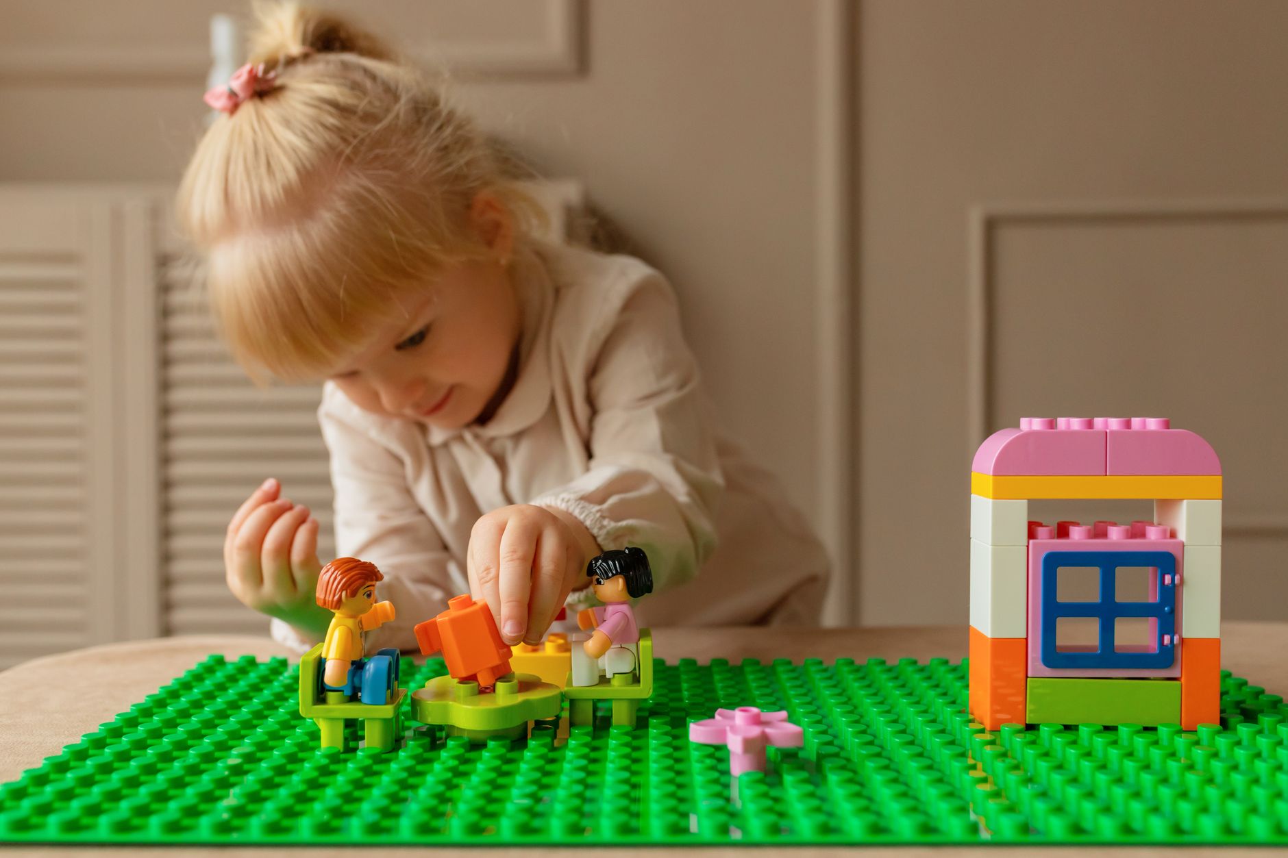 A young girl engaging creatively with colorful plastic building blocks on a table indoors.