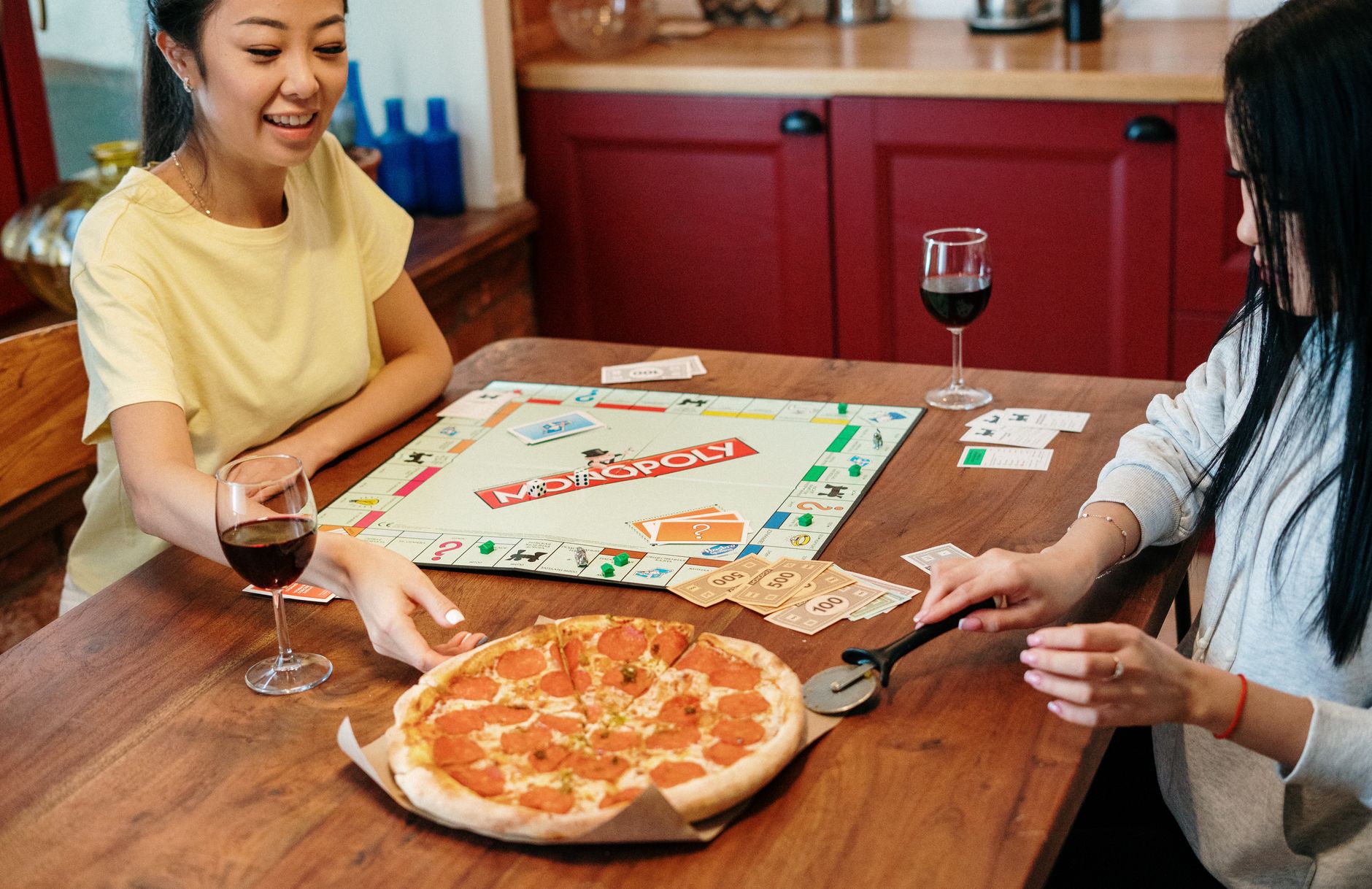 Two friends enjoying a cozy game night with Monopoly and pizza at home.