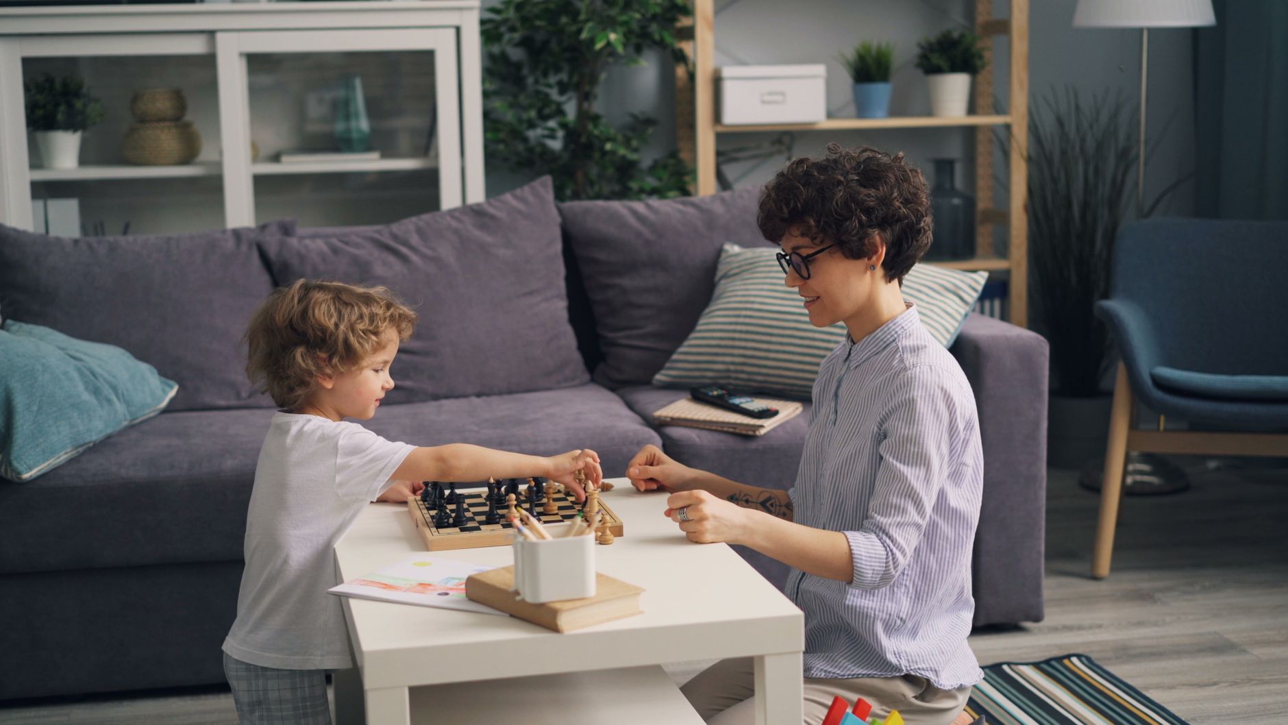 Child and adult engaged in a fun chess game together in a cozy living room setting.