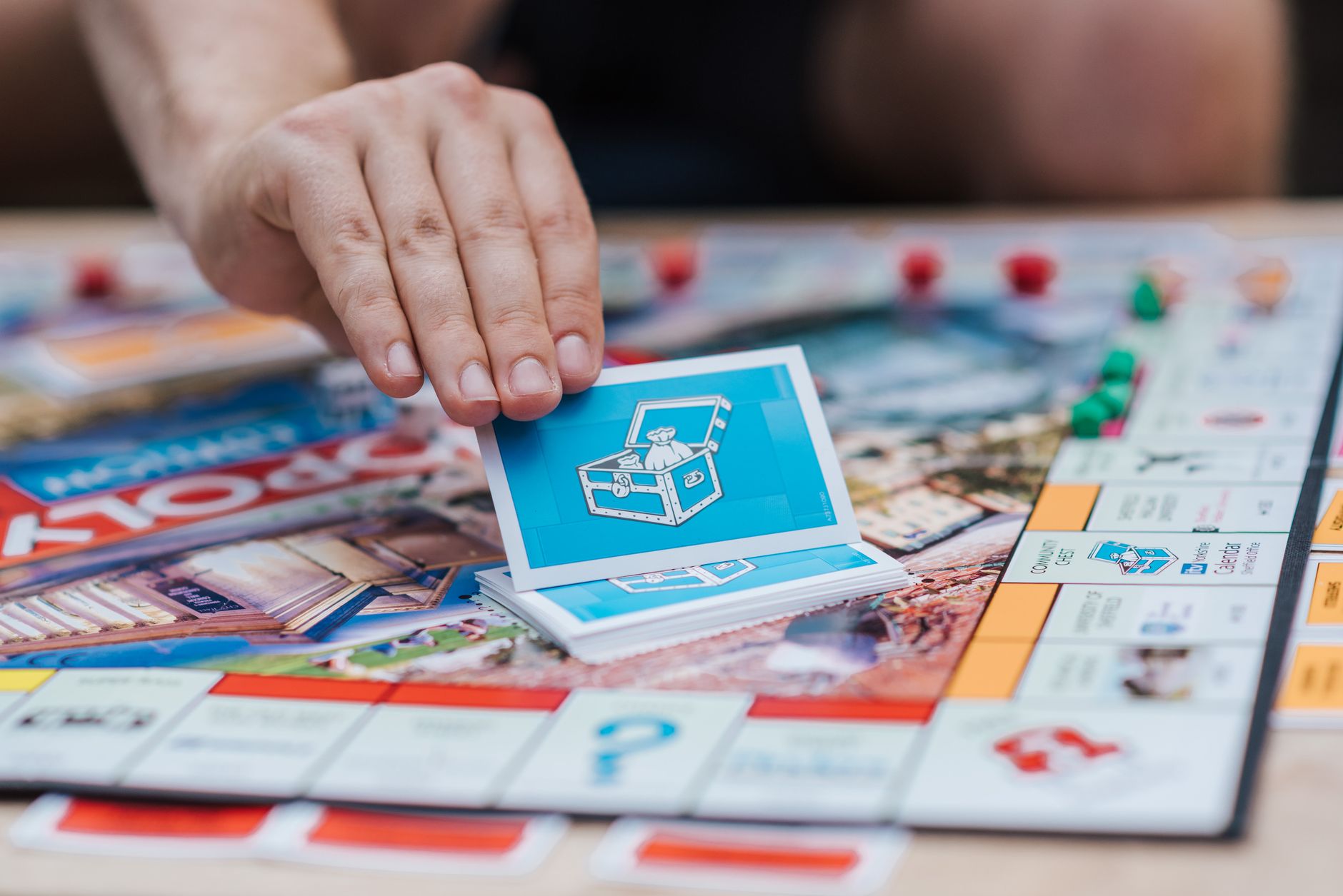 Crop unrecognizable person demonstrating game card with chest illustration while playing Monopoly on board