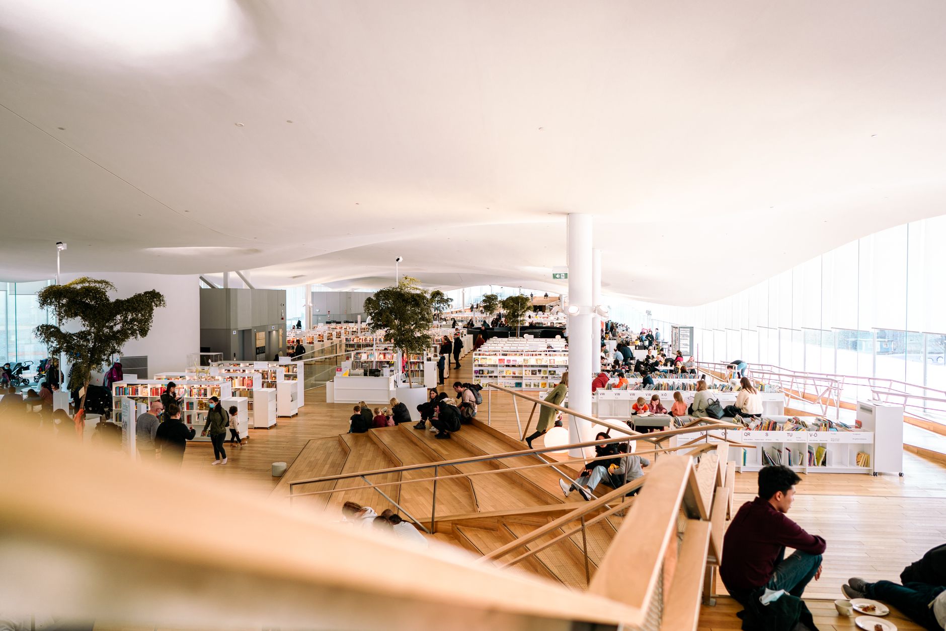 Contemporary library interior filled with people reading and relaxing in a bright and open space.