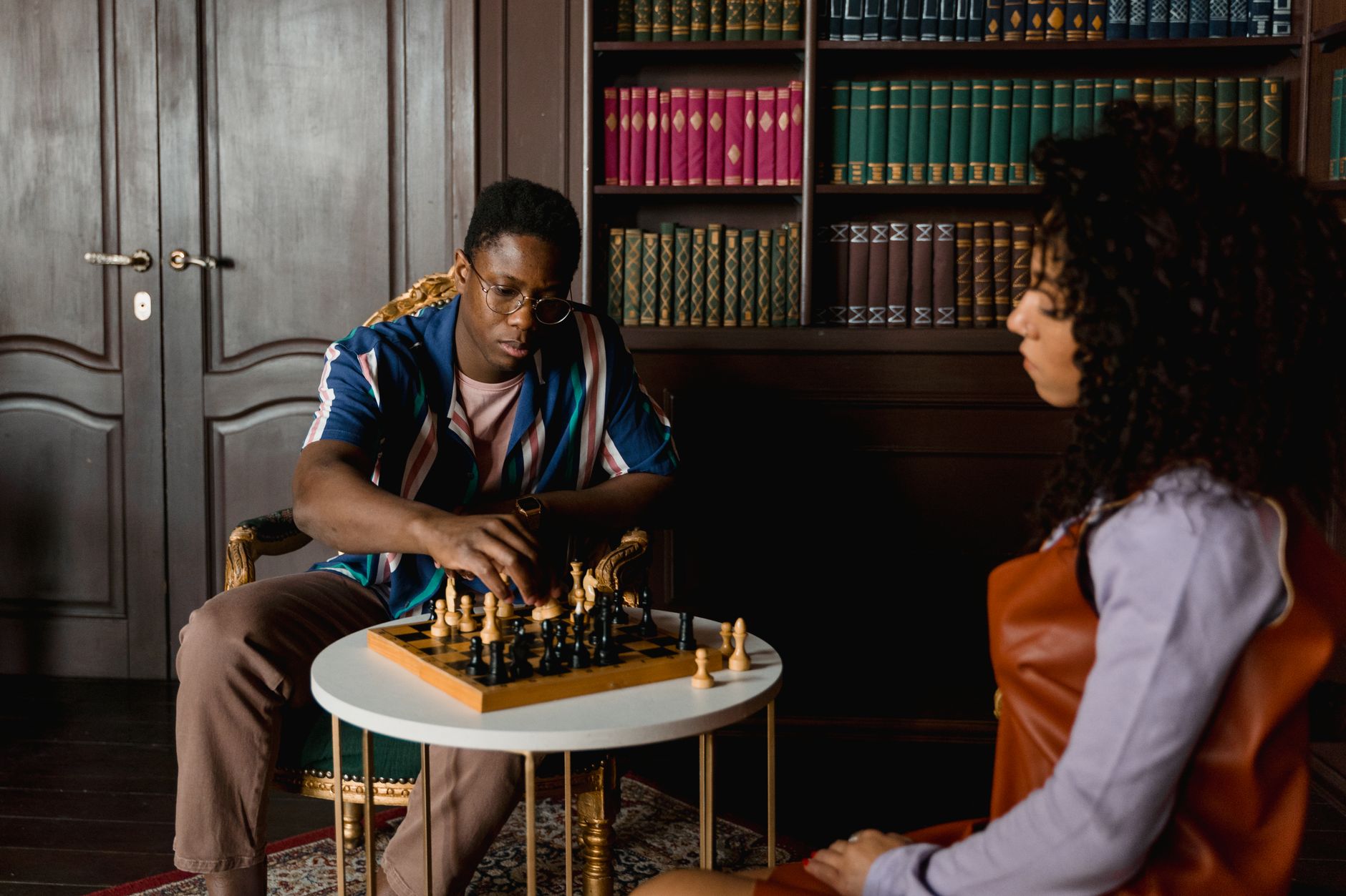 Two people playing chess in a warm, cozy library environment, focusing on strategy.