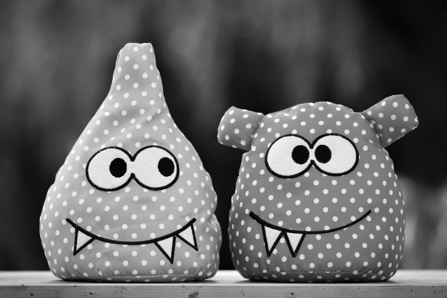 Two adorable polka dot plush monster toys with big eyes and fangs on a wooden surface.