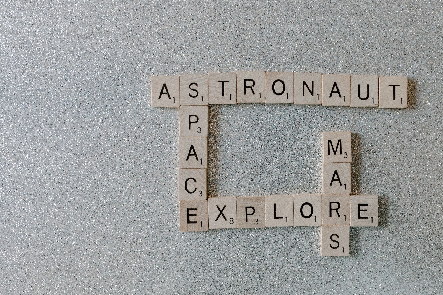 Wooden Scrabble tiles forming words related to space exploration on a glittery surface.