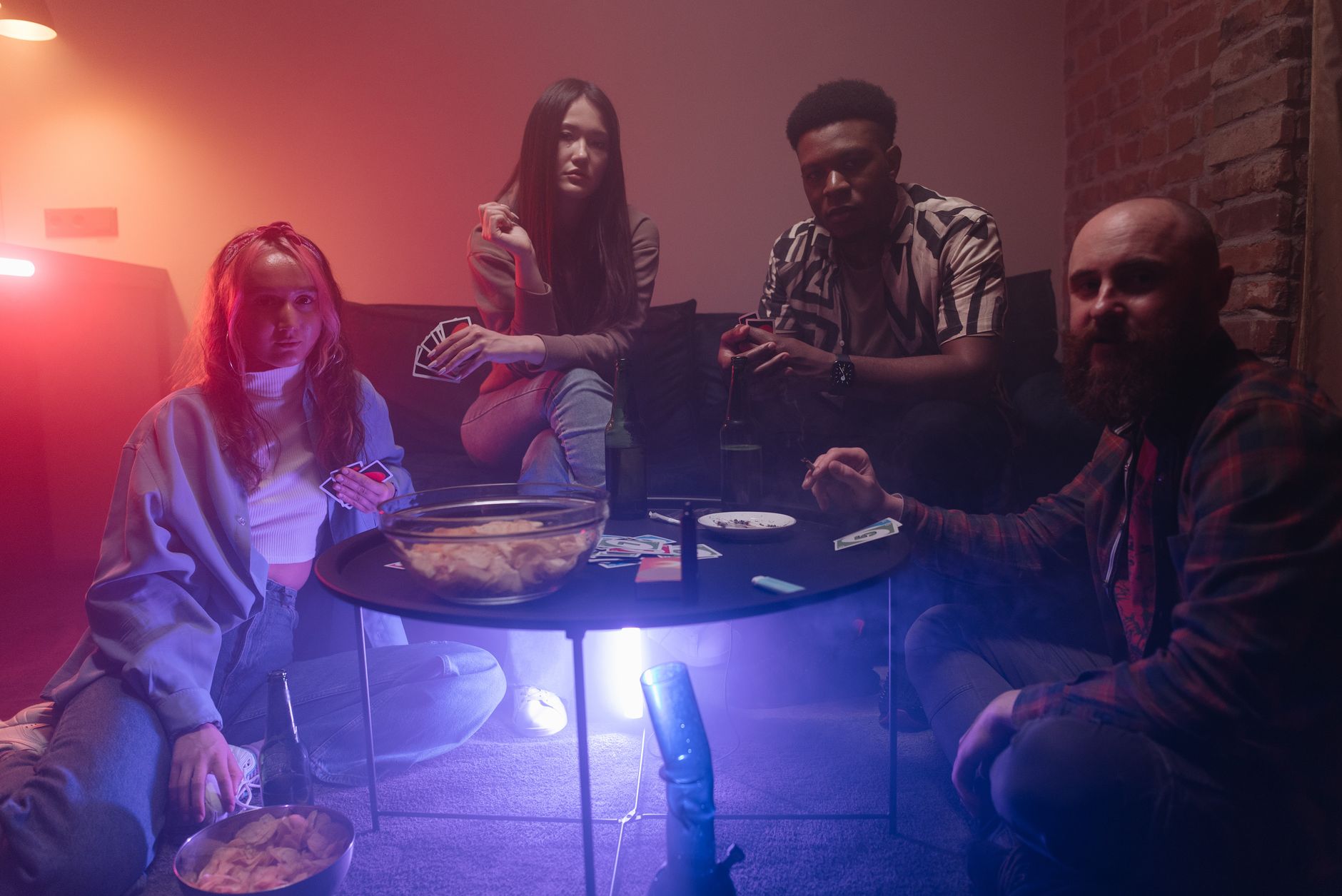 A group of diverse friends playing cards in an atmospheric indoor room with snacks and drinks.