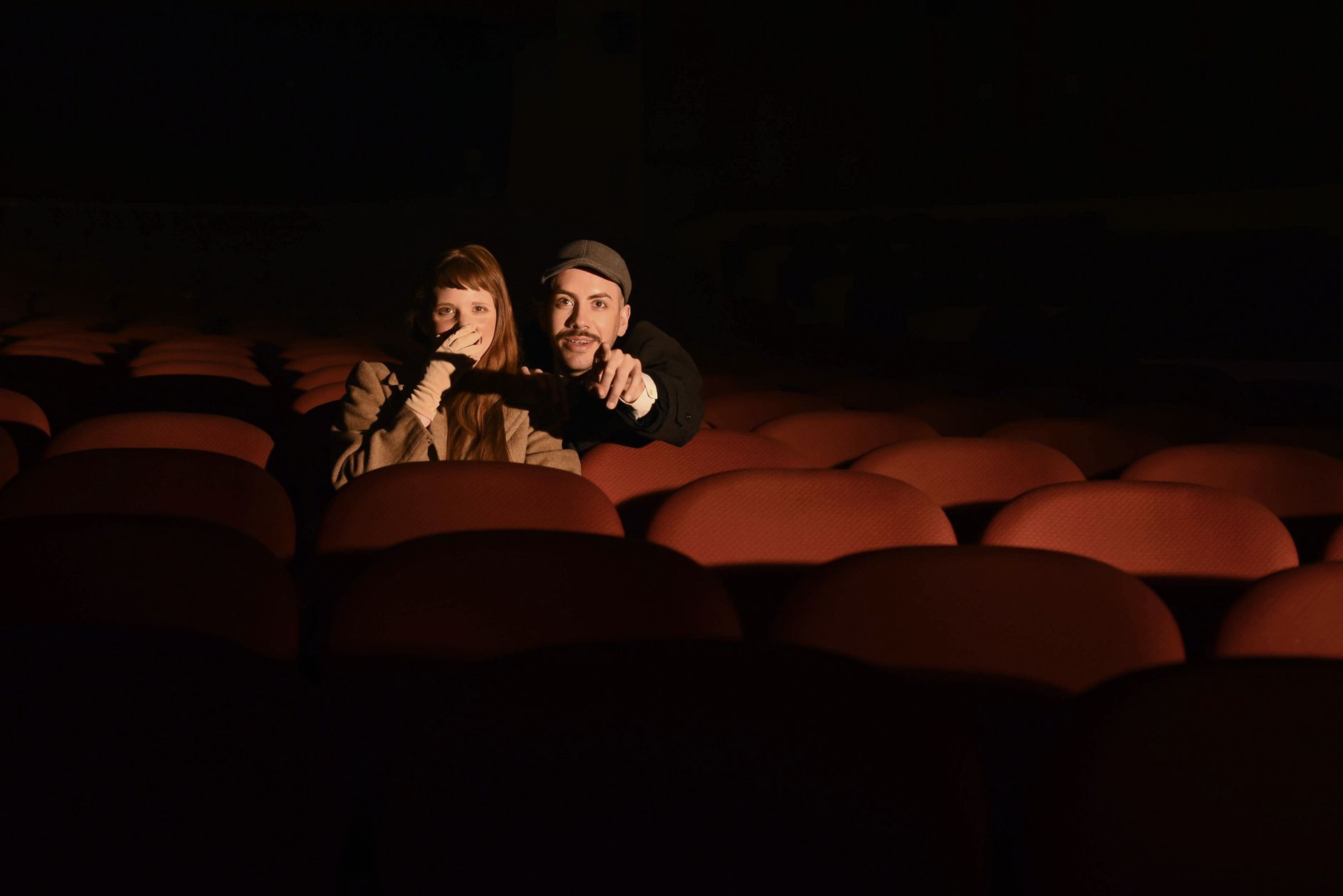A couple sits in a dimly lit cinema theater, enjoying a movie together.