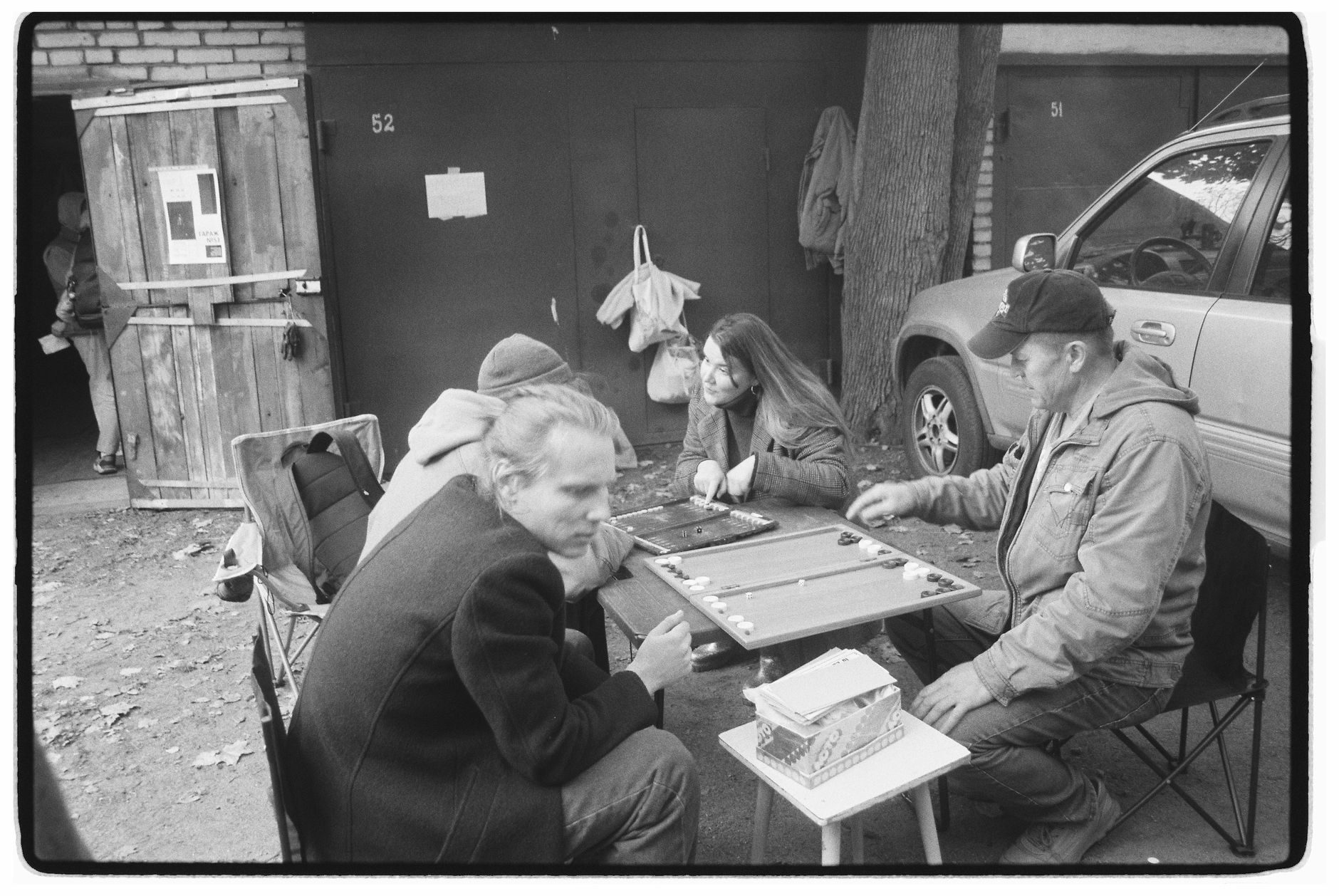 Black and white photo of adults playing a board game outdoors in an urban setting.